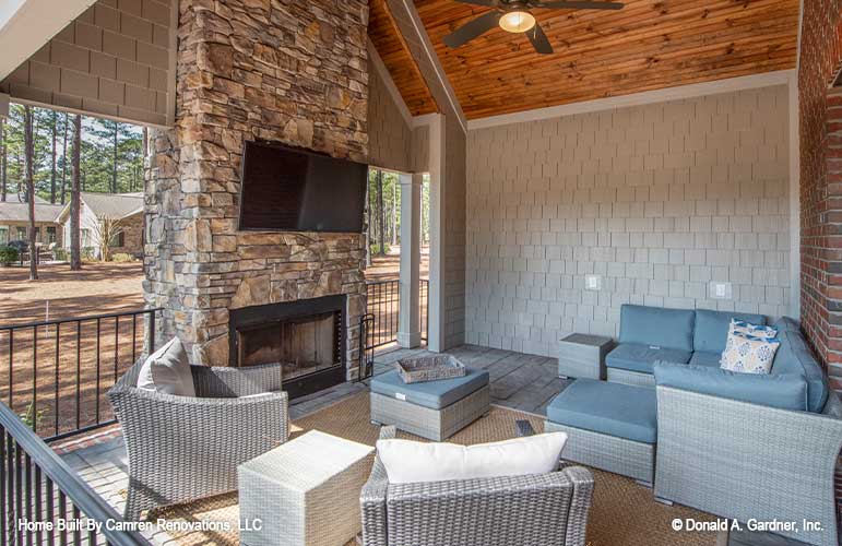 A fireplace provides warmth on chilly nights on the rear porch of one story house plan 1371 The Drake