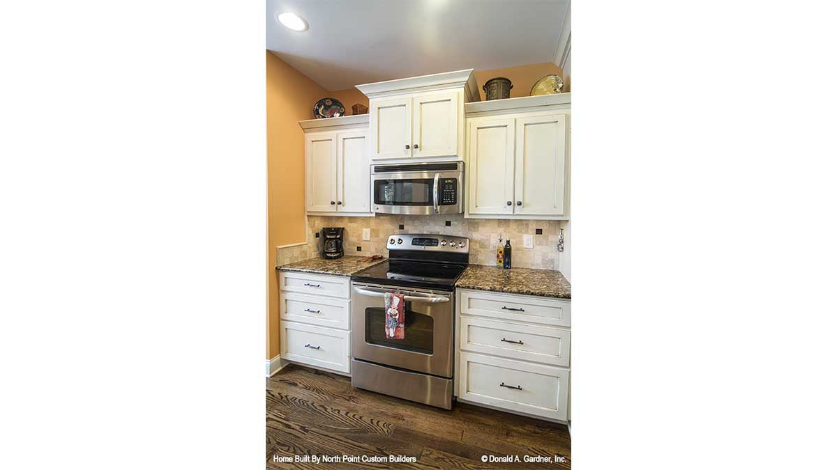 White cabinets and wood flooring in the kitchen. The Lisenby plan #1220.