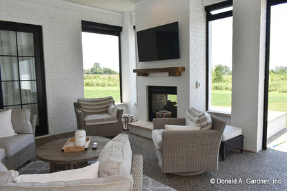 A cozy fireplace warms the rear porch of one story house plan 1378 The Roseburg