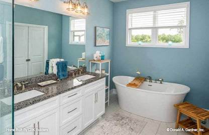 Double sink vanity along side a stand alone soaking tub with window above. Sloan plan 1528