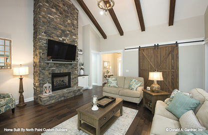 Floor to ceiling stone fireplace and stained wood beams on the ceiling in the great room. The Wilkerson plan 1296.