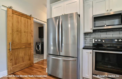 Kitchen view of the double door stainless steel fridge and utility room with sliding farmhouse door. The Wycliff plan